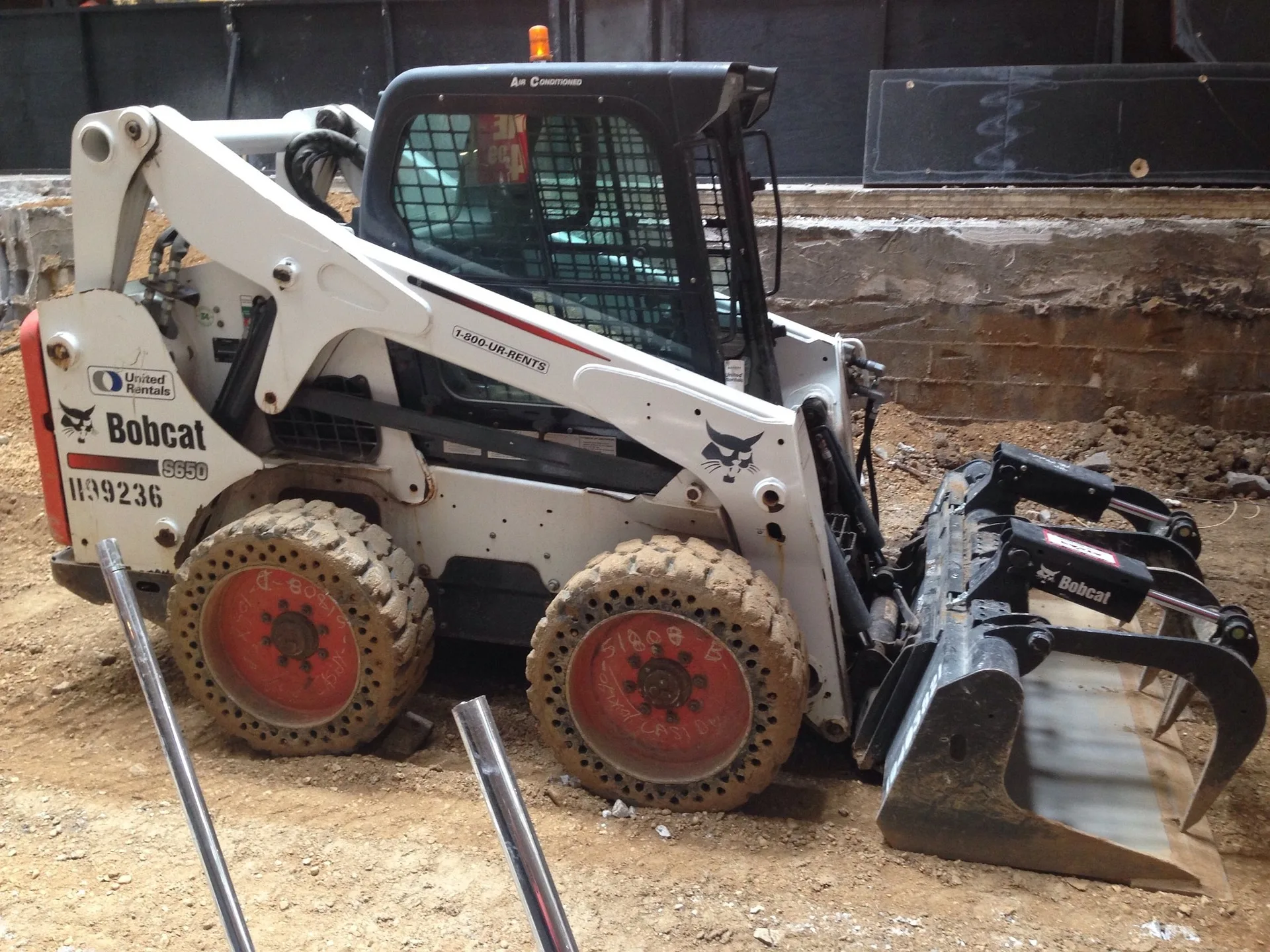 Bobcat skid-steer loader with a debris grapple attachment on an excavation site.